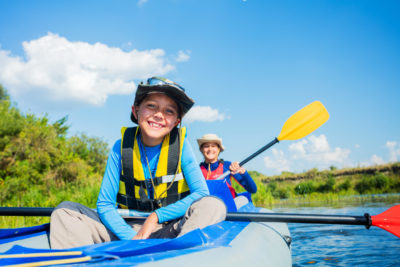 A young smiling boy and woman enjoying the river in an inflatable raft in plentiful sunshine.