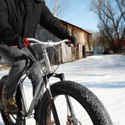 Man in black winter jacket riding a Fat Tire Snow Bike near and old building on Treetops Resort bike trails in Gaylord, Michigan