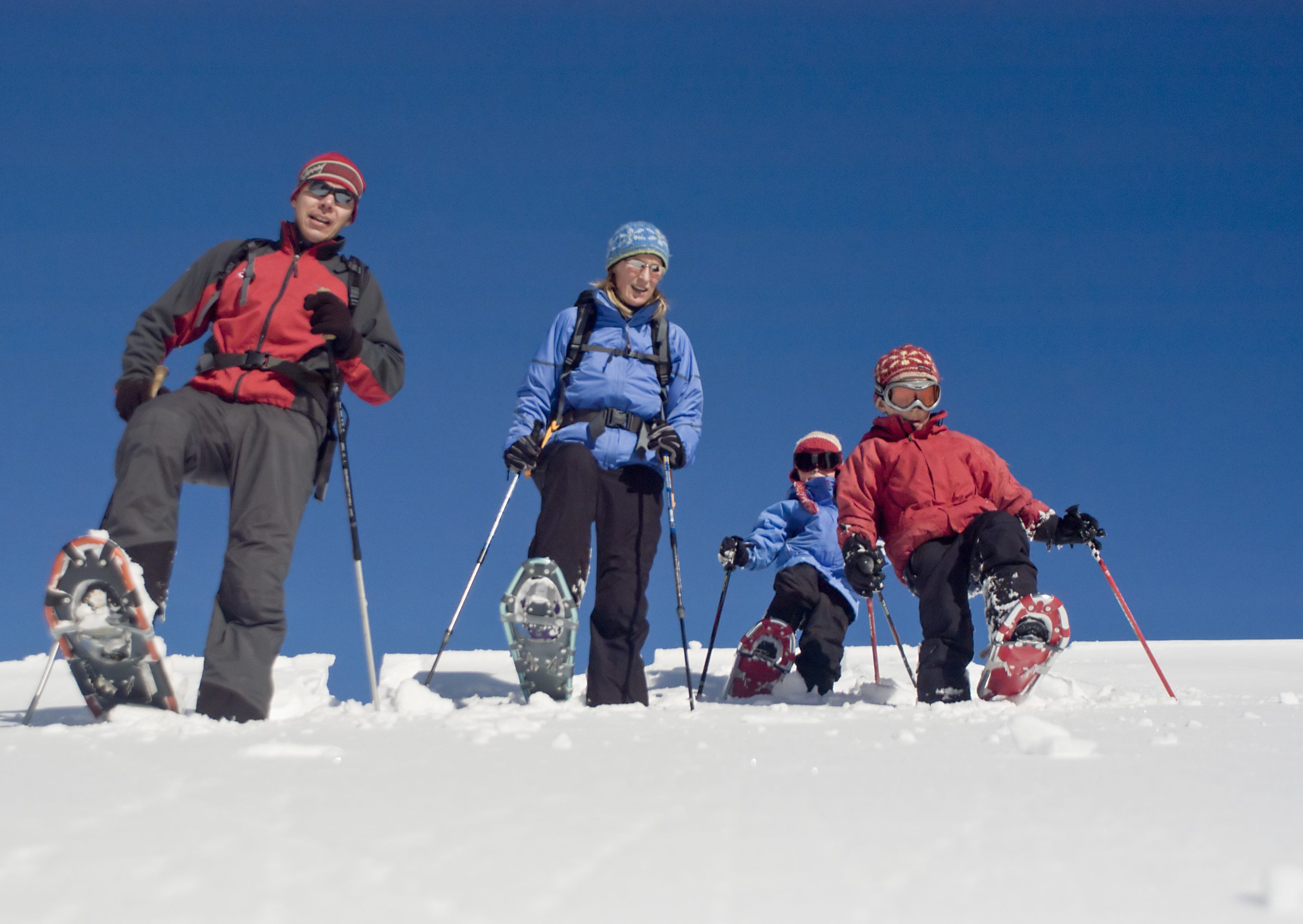 A family of four enjoys a snowshoeing excursion on a bright, sunny day.