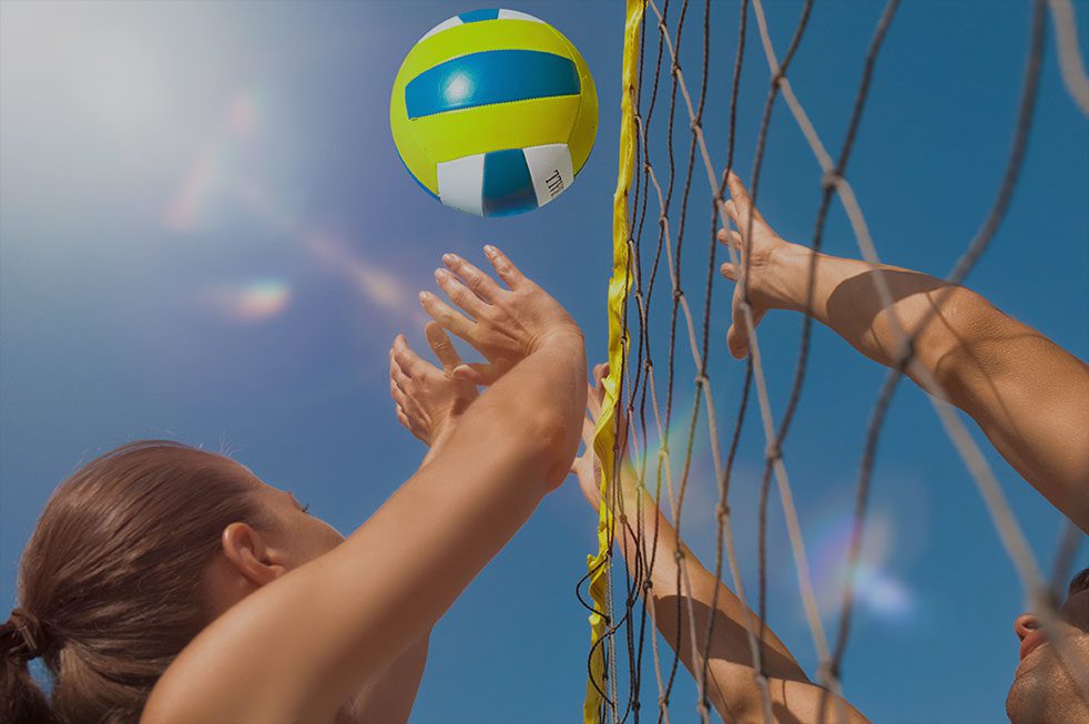 Two people jumping with arms up at the volleyball net.