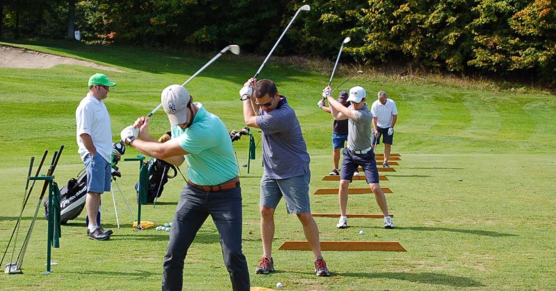 Group of golfers swing on the Treetops golf course driving range with Gaylord Stay and Play golf packages
