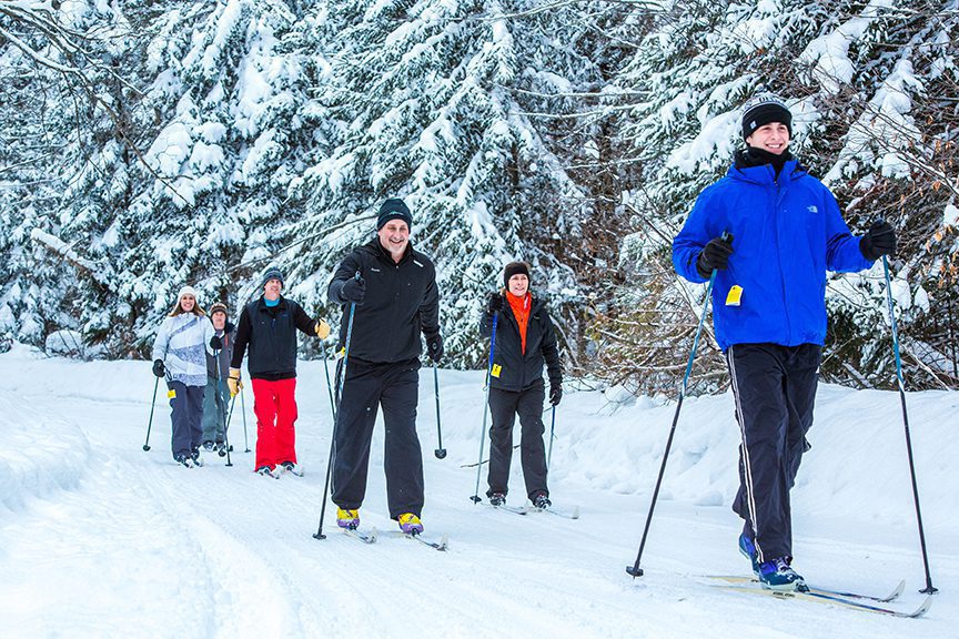 A group of people smiling while cross country skiing through the snow.