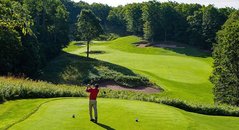 A mean wearing a red shirt and khaki pants tees off at Treetops Resort. Find how to fix a slice in golf.