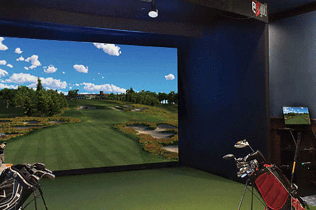 The indoor golf simulator screen at Treetops Resort with bags of golf clubs, ready to play.