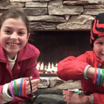 Two smiling children sit next to a fireplace with several bracelets on their arms at Treetops Resort.