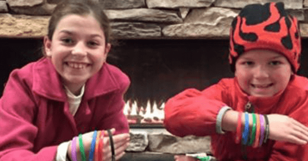 Two smiling children sit next to a fireplace with several bracelets on their arms at Treetops Resort.