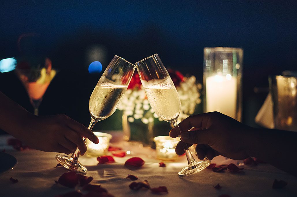 Two champagne glasses toasting with candles and roses on the table