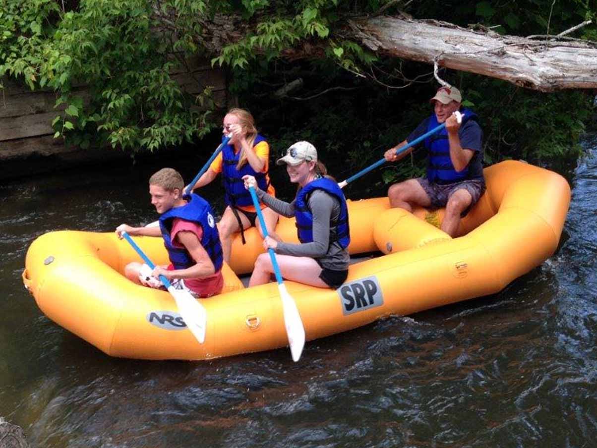 Four people enjoy a rafting trip on a Michigan river while visiting golf resort Michigan Treetops