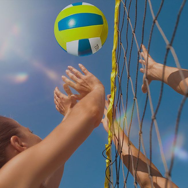 Two people jumping with arms up at the volleyball net.